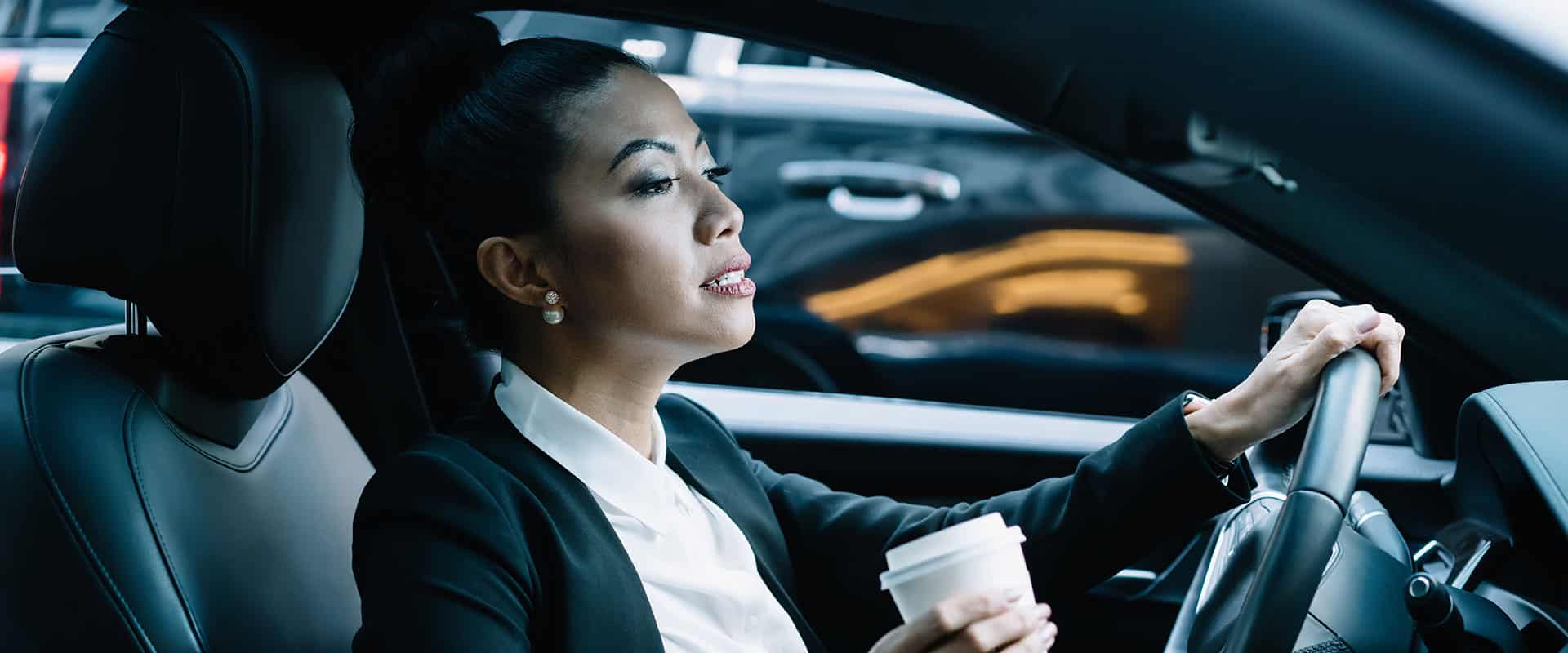 A woman driving a car holding a cup of coffee.